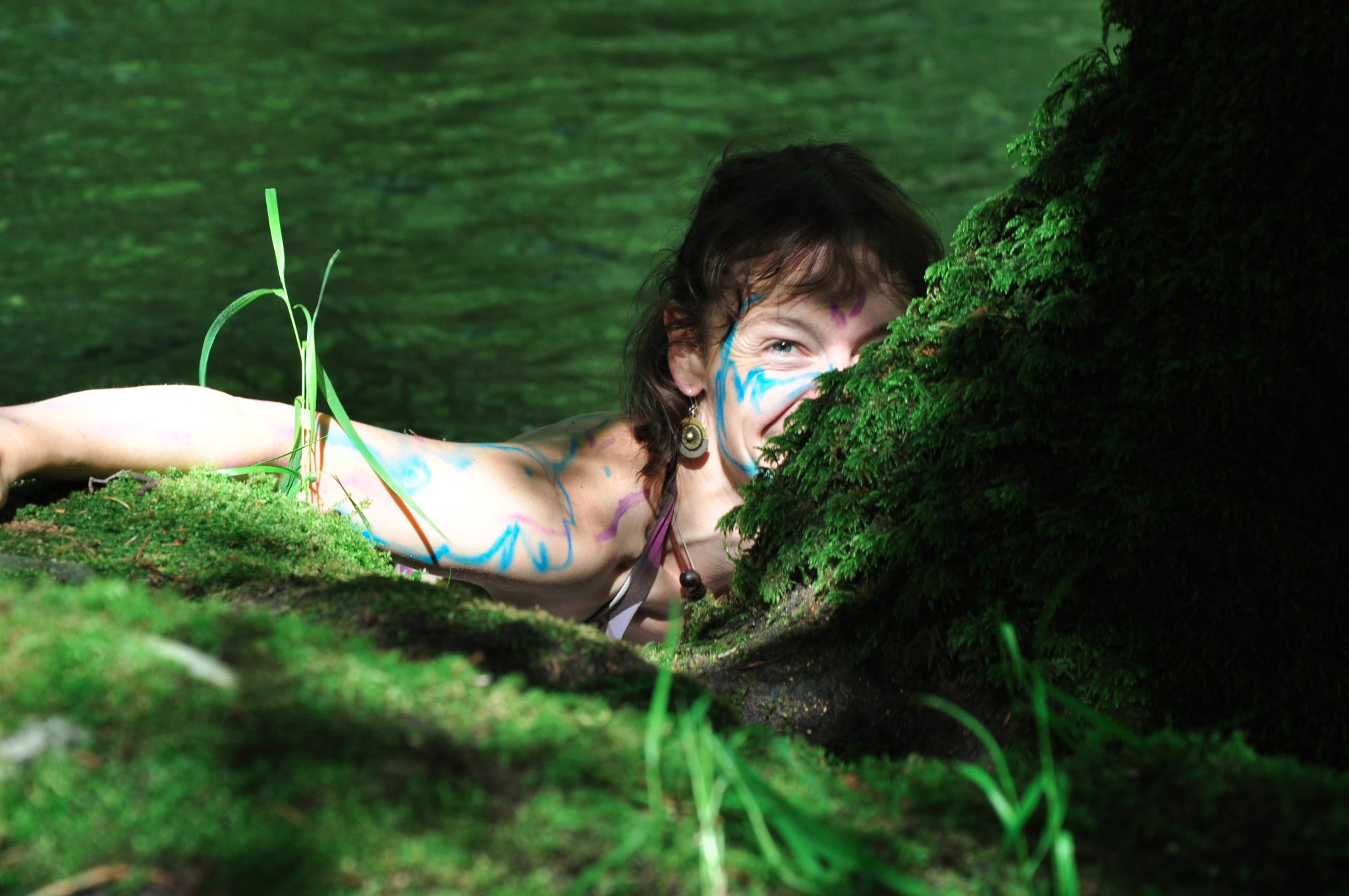 une femme heureuse est dans la nature. on voit des arbres, de la mousse et de l'eau.